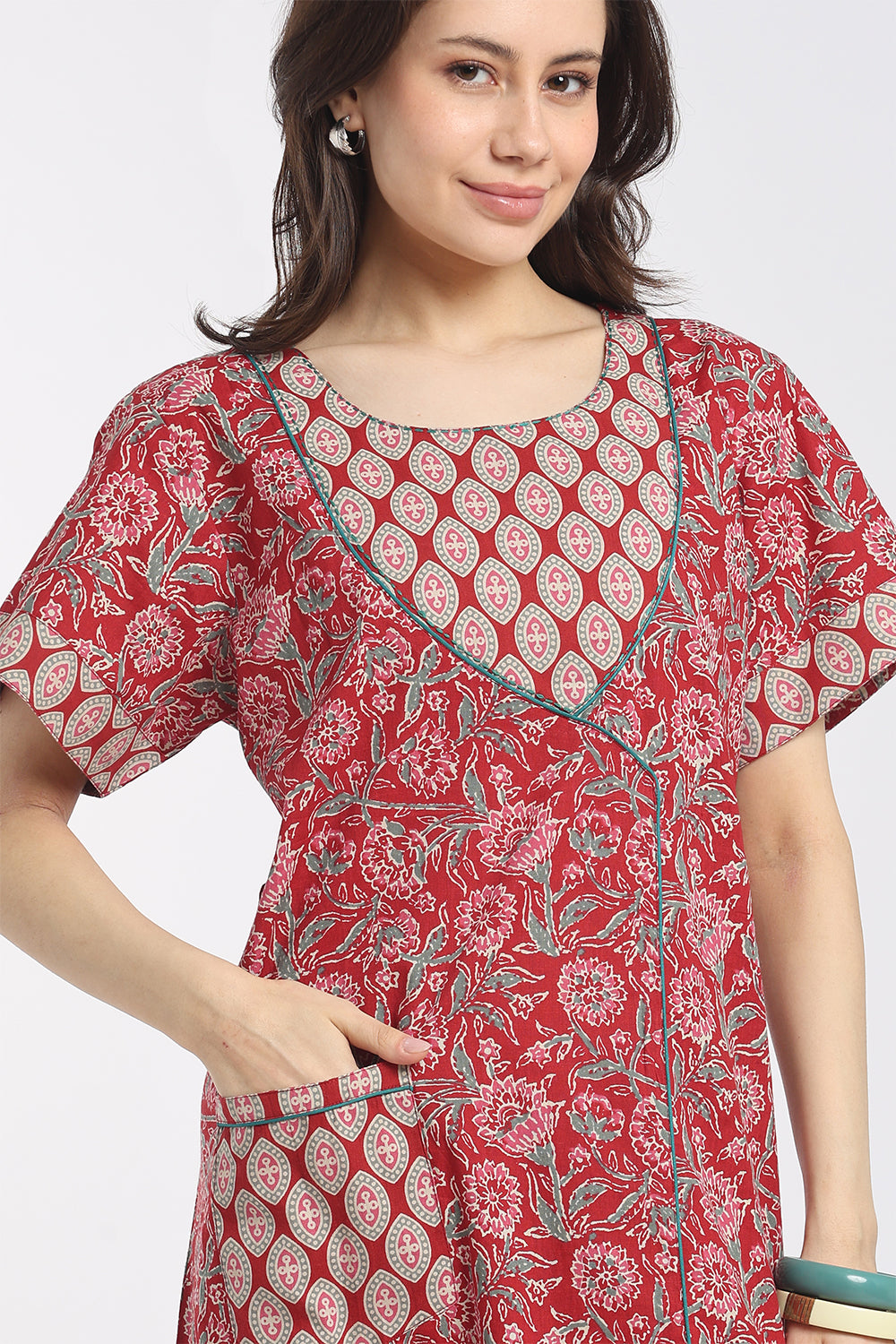 A woman wearing a red short-sleeve tunic dress with a white and gray floral block print pattern, featuring a round neckline and a front patch pocket.