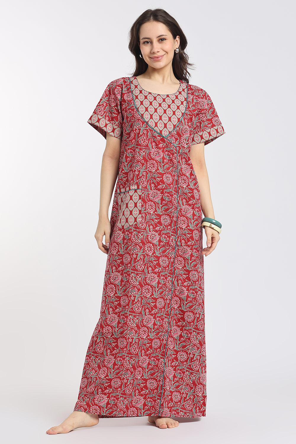 A woman modeling a long red and pink floral print maxi dress with short flutter sleeves and a V-neckline, photographed against a plain light gray studio background.