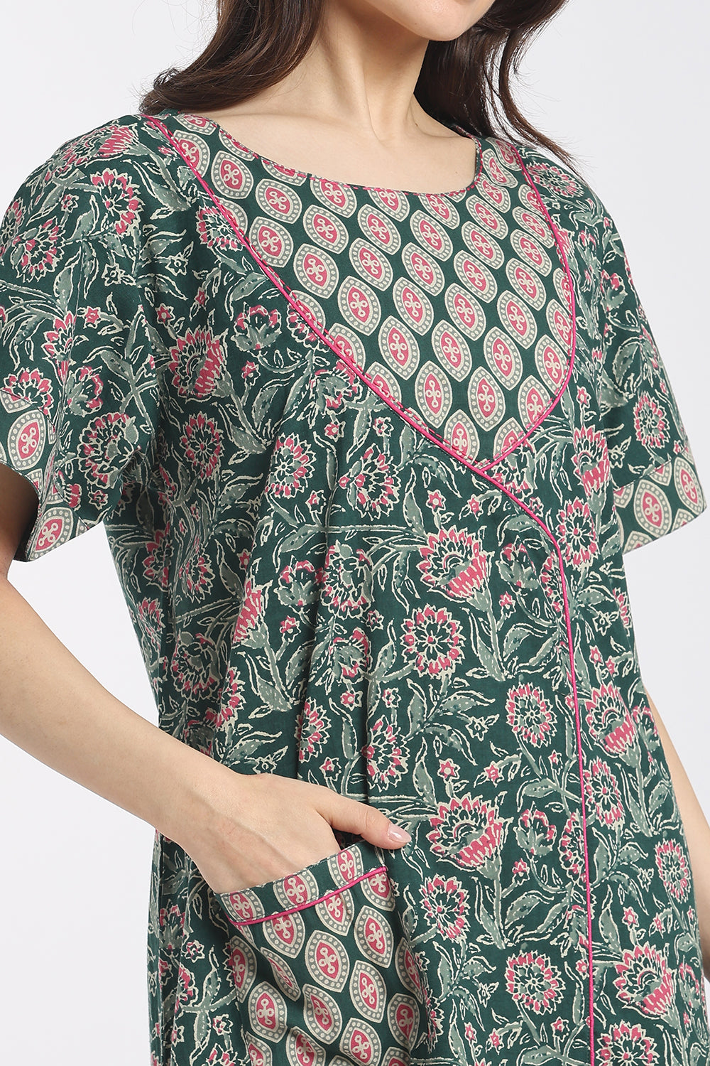 A close-up of a woman wearing a dark green short-sleeve dress with a pink and white floral block print pattern and pink contrast piping.
