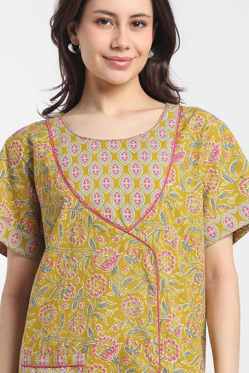 A woman wearing a mustard yellow short-sleeve tunic top with a pink and green floral block print and pink piping trim.