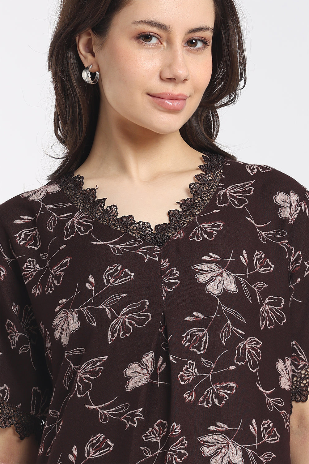 A close-up of a woman wearing a dark brown short-sleeve top with a light pink floral line print and a black lace V-neck trim.