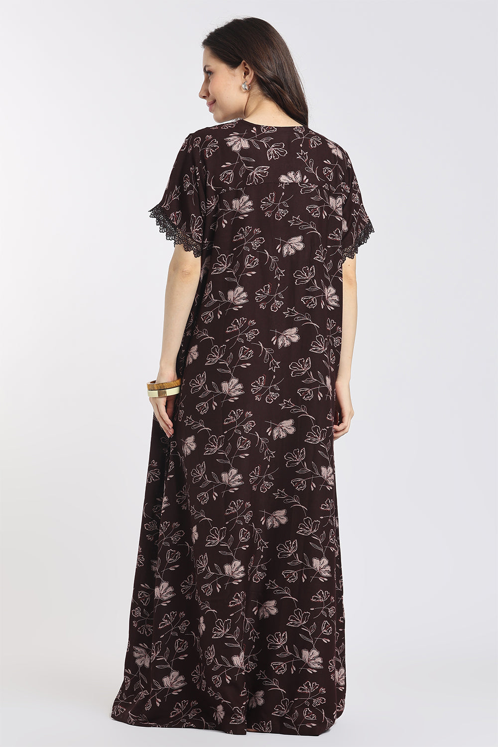 A woman modeling a long dark brown maxi dress with a light brown floral pattern, shown from the back against a plain white studio background.
