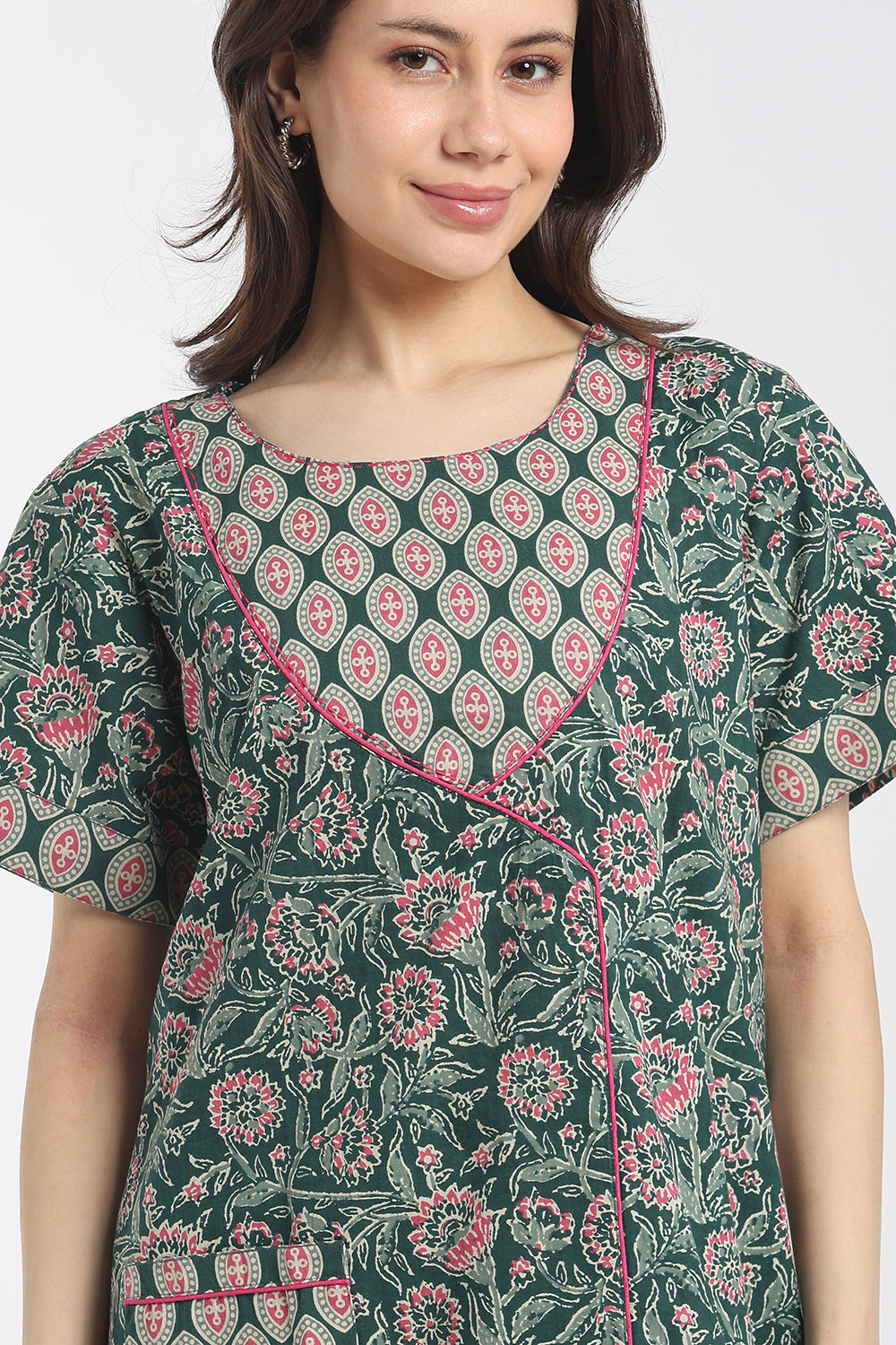 A woman wearing a dark green short-sleeve tunic top with a pink and white floral block print and pink piping along the neckline.