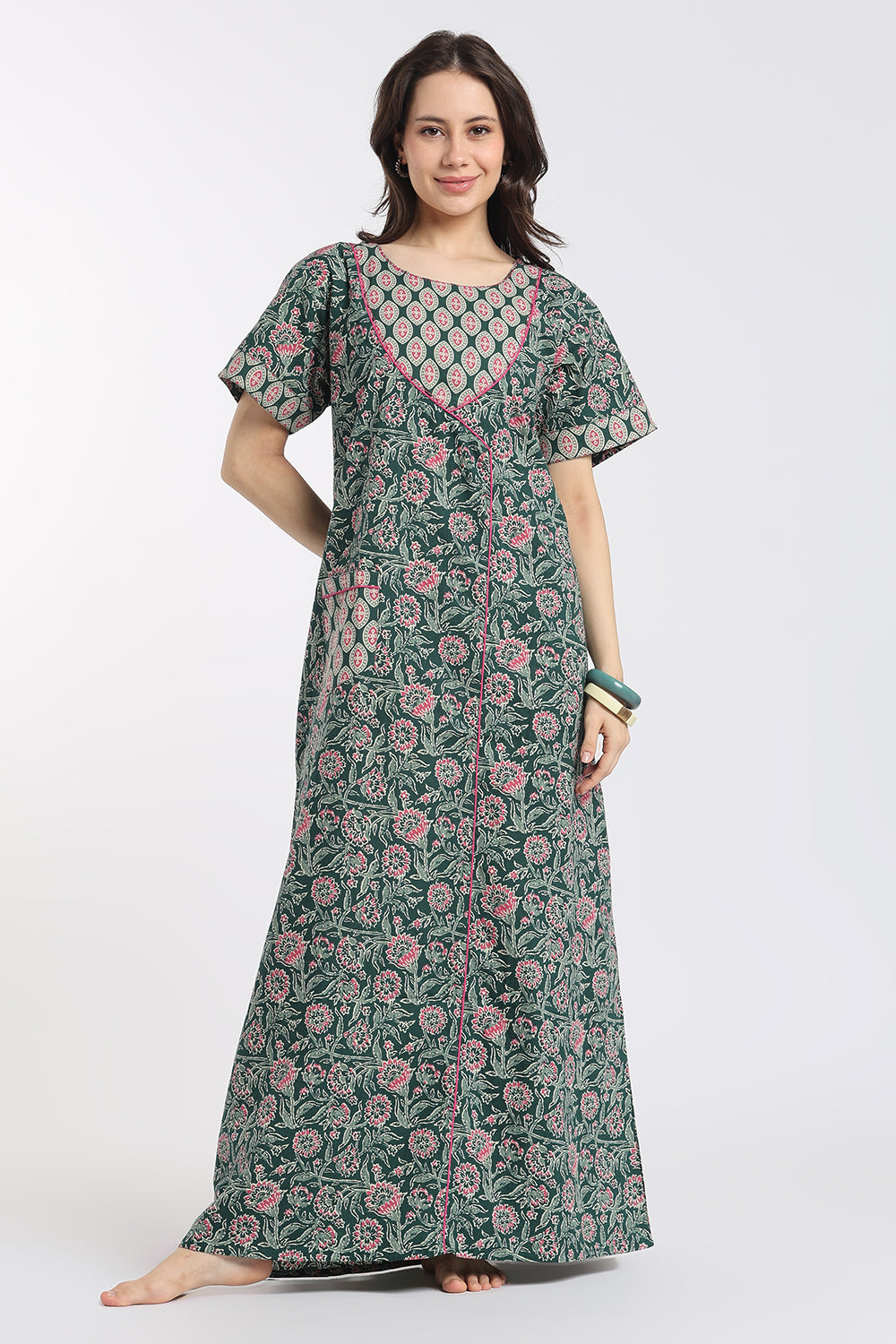 A woman modeling a long-sleeved, floor-length floral print nightgown or kurta in green, pink, and white, standing against a plain light gray studio background.