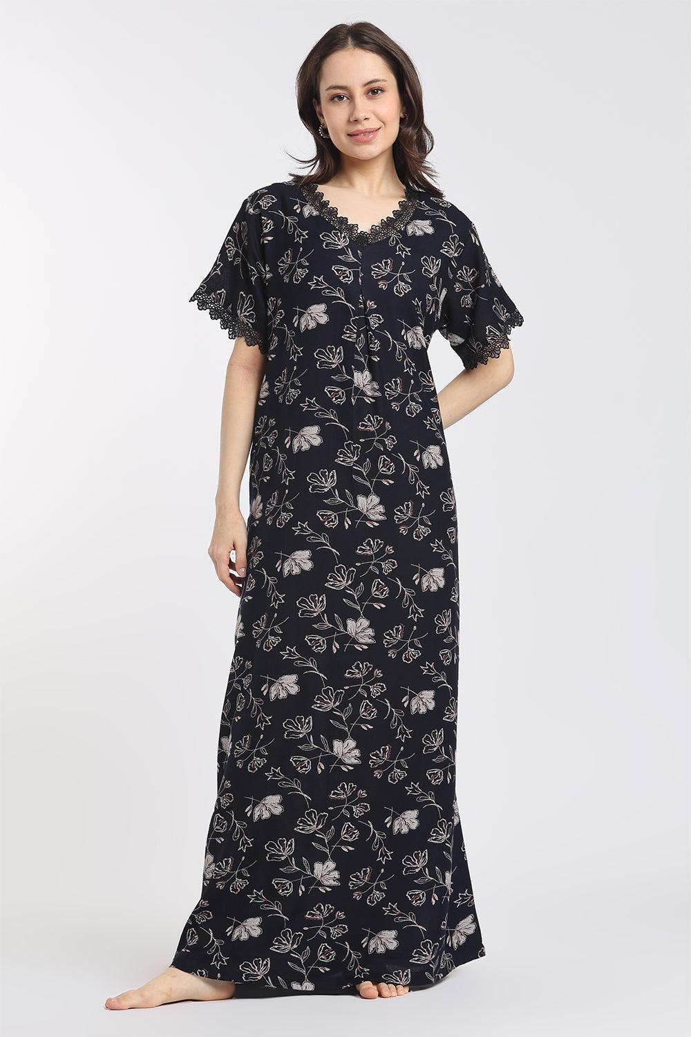 A woman modeling a long black nightgown with a white floral print, featuring flutter sleeves and a scalloped neckline, against a plain light gray background.