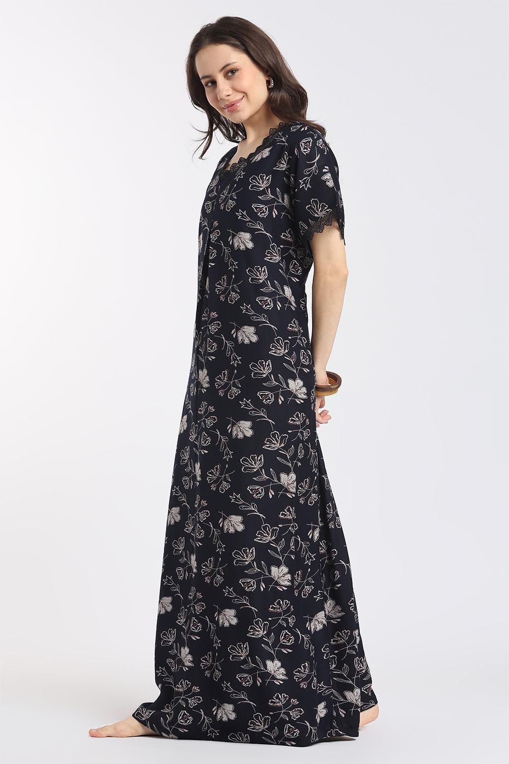 A woman modeling a long black maxi dress with a white floral print, standing against a plain white studio background.